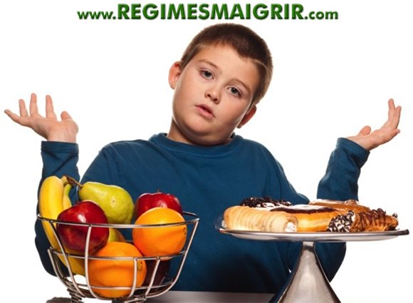 Un garçon en surpoids hésite entre des fruits et des gâteaux très caloriques