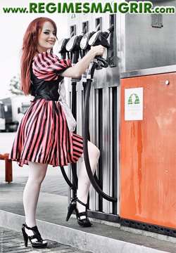 Une femme portant une robe sourit tout en prenant une pompe dans une station d'essence