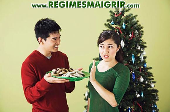 Un homme essuie le refus d'une femme à consommer un plat apparemment sucré devant le sapin de Noël