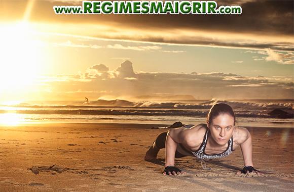 Une femme est en train de faire un exercice cardio classique que sont les pompes sur une plage sablée