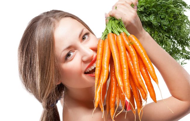Une femme sourit tout en tenant une douzaine de carottes fraches