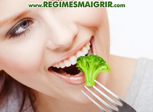 Une jeune femme dguste du brocoli tout en souriant