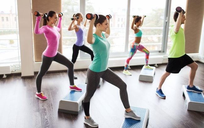 Plusieurs femmes lvent un haltre au-dessus de leur tte derrire un instructeur de sport