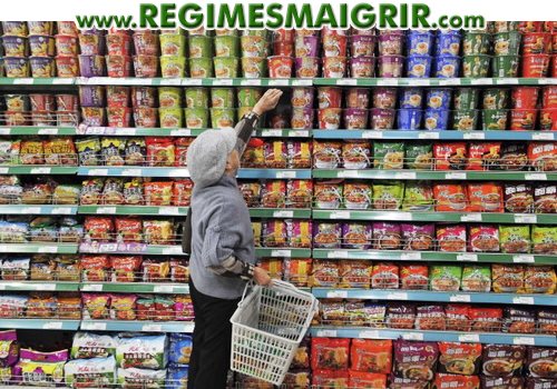 Une femme fait ses courses dans un rayon de supermarché rempli de paquets et de gobelets de nouilles consommables momentanément