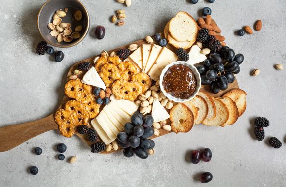 Un plateau de fromages avec des raisins noirs, des myrtilles, des crackers, des amandes et du pain