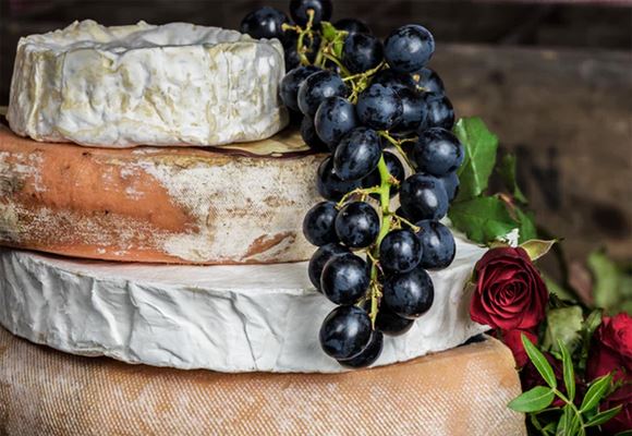 Une grappe de raisins noirs pose sur une pile de fromages et  ct de deux roses rouges