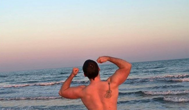 Un homme montre ses muscles de dos devant la mer