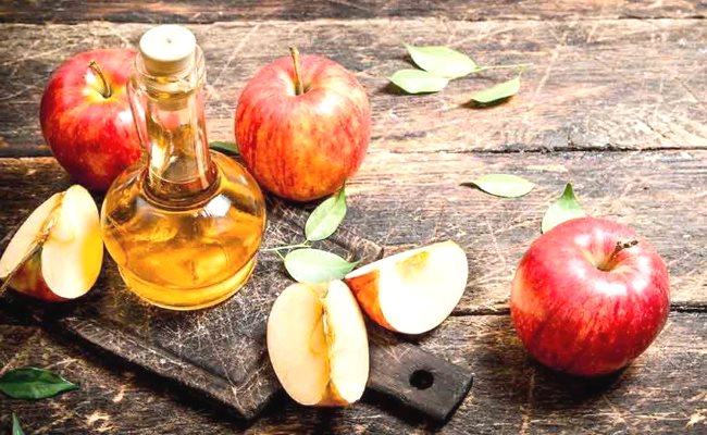 Une bouteille de vinaigre de cidre pose sur une table en bois