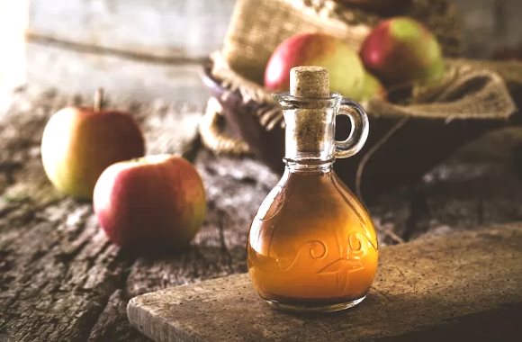 Une bouteille de vinaigre de cidre est pose sur une table en bois  ct de plusieurs pommes